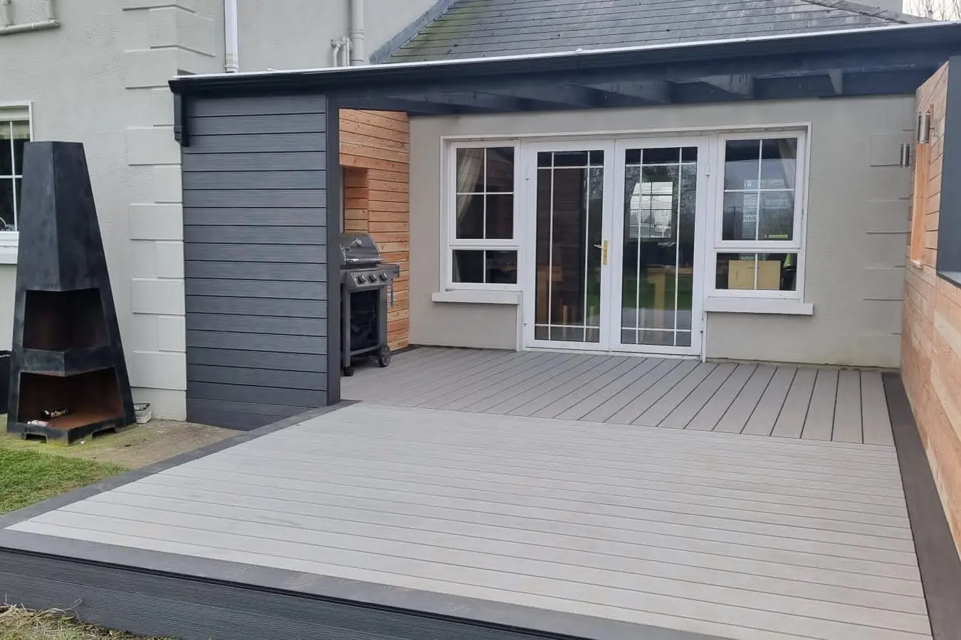 After: light grey composite deck with a charcoal frame and a larch wall, Tipperary